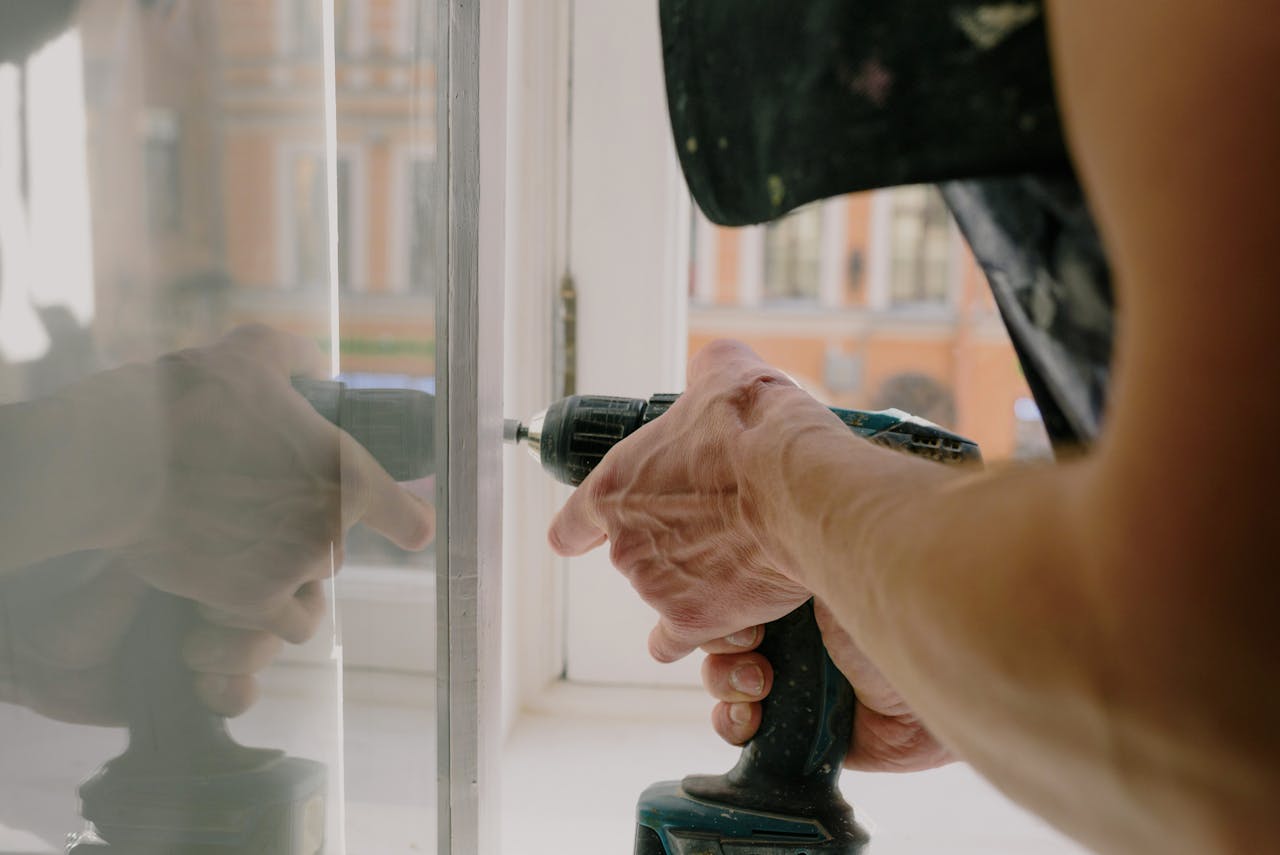 hero-services Close-up of a handyman's hands using a drill to fix a window inside an apartment.
