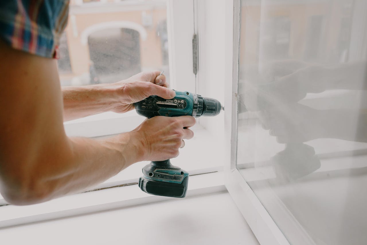 hero-contact A person using an electric drill to repair or install a window indoors.
