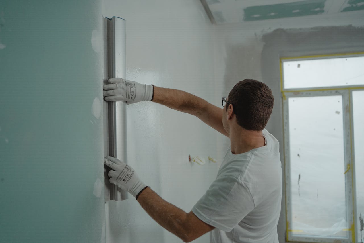 hero-homepage A man in a white shirt and gloves using a metal ruler for indoor wall renovation work.