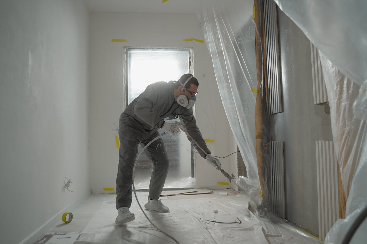 about-02 A worker in protective gear painting walls during an indoor renovation project.